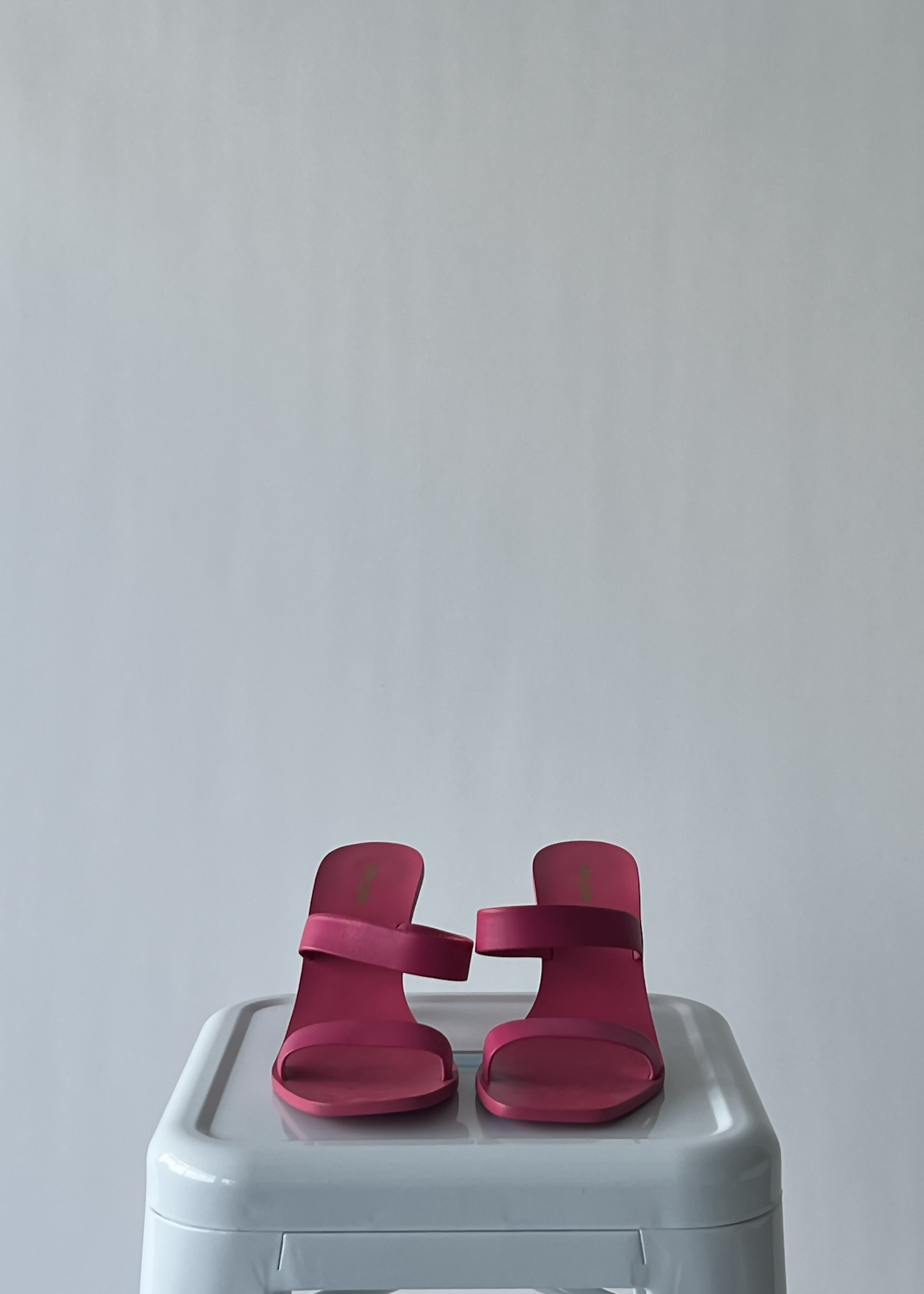 A pair of brand new Cult Gaia Barbie Pink heels from EXCHANGE sit side by side on a white rectangular stool, set against a plain light gray background.