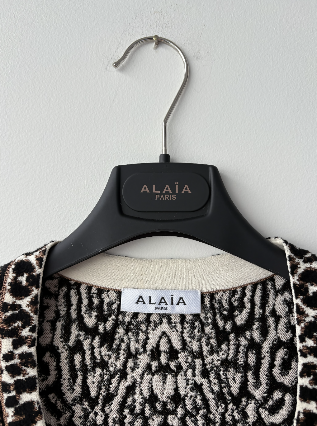 A close-up of a black hanger labeled EXCHANGE STORE holding the Alaia Leopard-print Jacquard Minidress, with its tag visible and sculpting fit on display against a white wall.