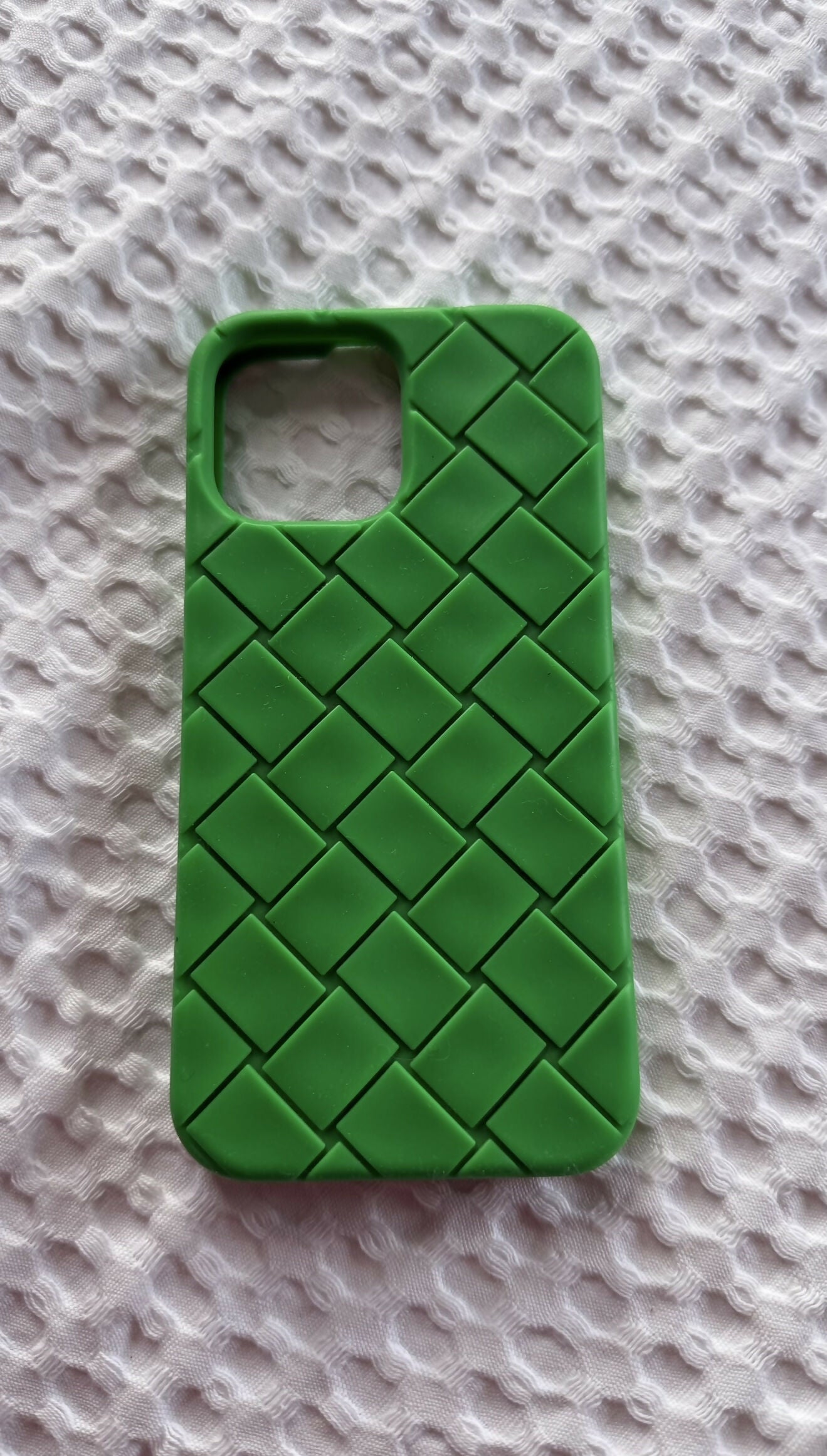 An EXCHANGE STORE Intrecciato Rubber iPhone 13 Pro Max Case in Parakeet Green with a raised crisscross diamond pattern rests on a white textured fabric surface.
