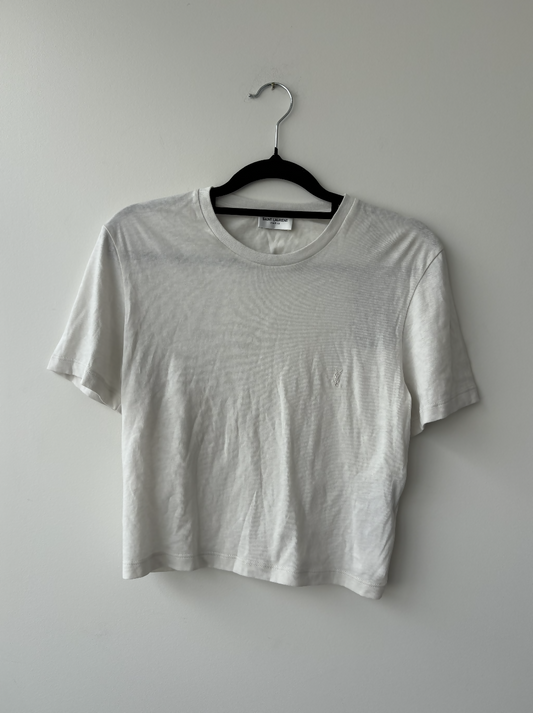 The Yves Saint Laurent Beige Logo Cropped T-Shirt from EXCHANGE STORE, featuring short sleeves, is displayed on a black plastic hanger against a light wall.