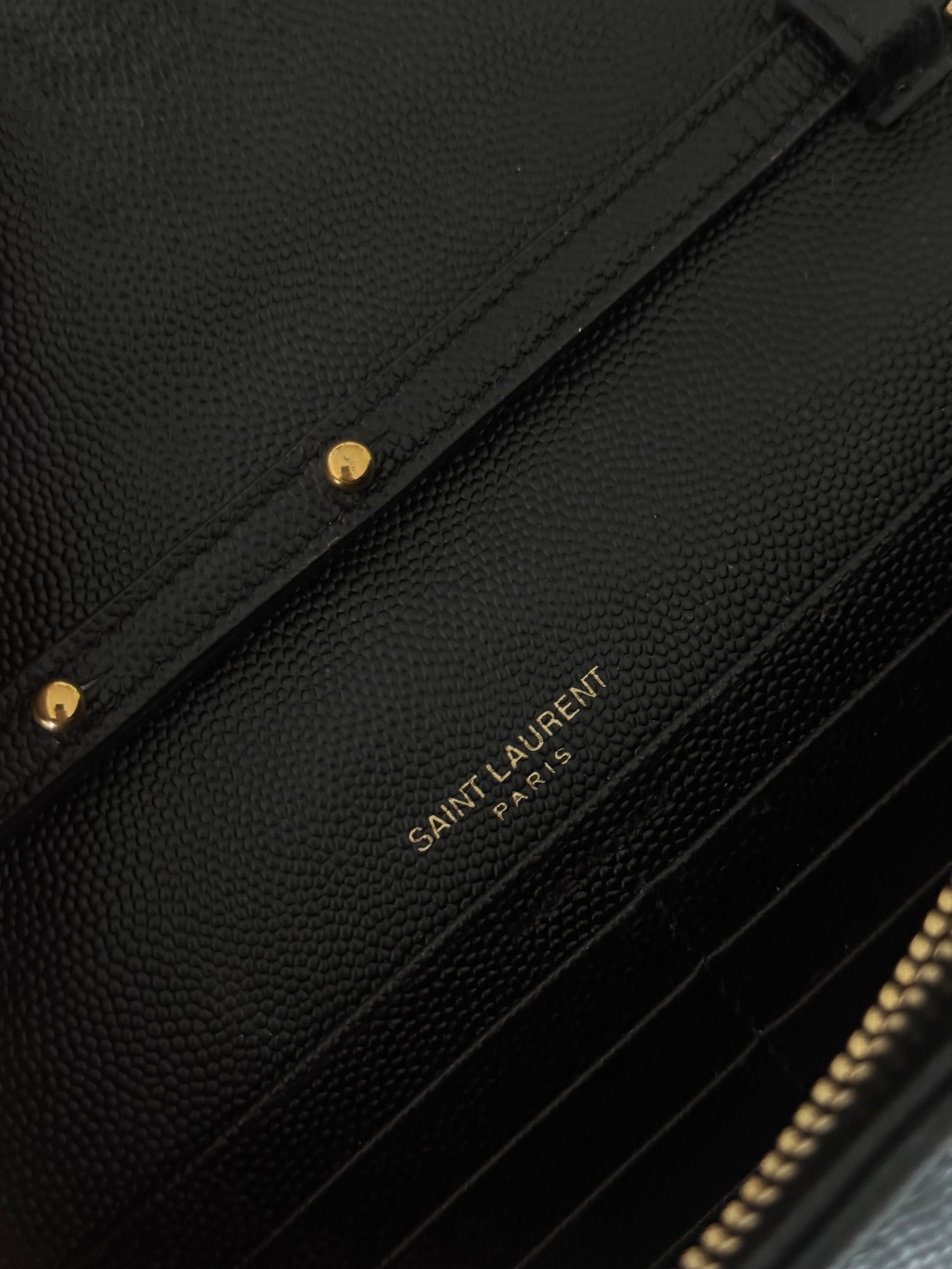 Close-up of a Saint Laurent Classic Cassandre chain wallet in grain de poudre leather by EXCHANGE STORE, black with textured finish, gold hardware, chevron quilting, and gold-embossed branding.