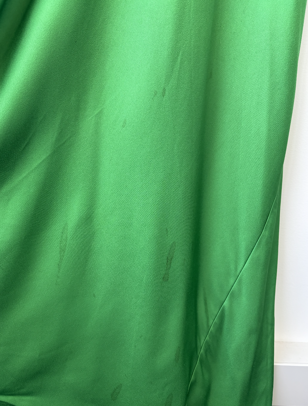 A Victoria Beckham Resort 2022 Green Cami Slip Dress from EXCHANGE STORE, featuring small irregular dark stains near the bottom and middle, illuminated by natural light coming from the right side.
