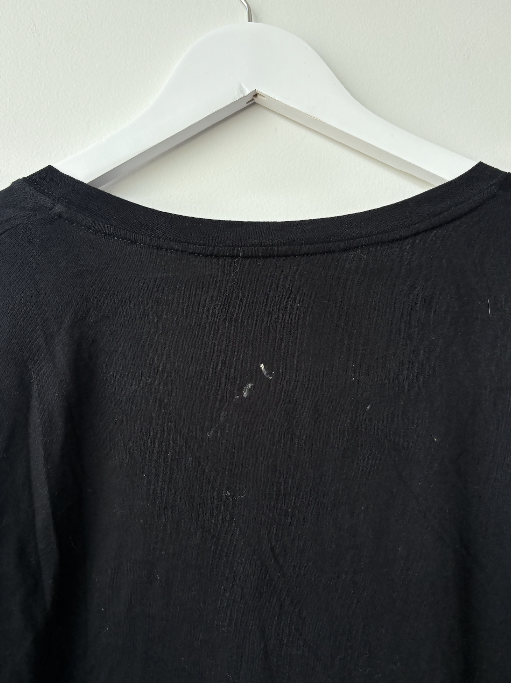 A close-up of the back of an EXCHANGE STORE Gucci Black L'Aveugle Par Amour T-Shirt on a white hanger, highlighting faint white marks and minor lint on the premium fabric.
