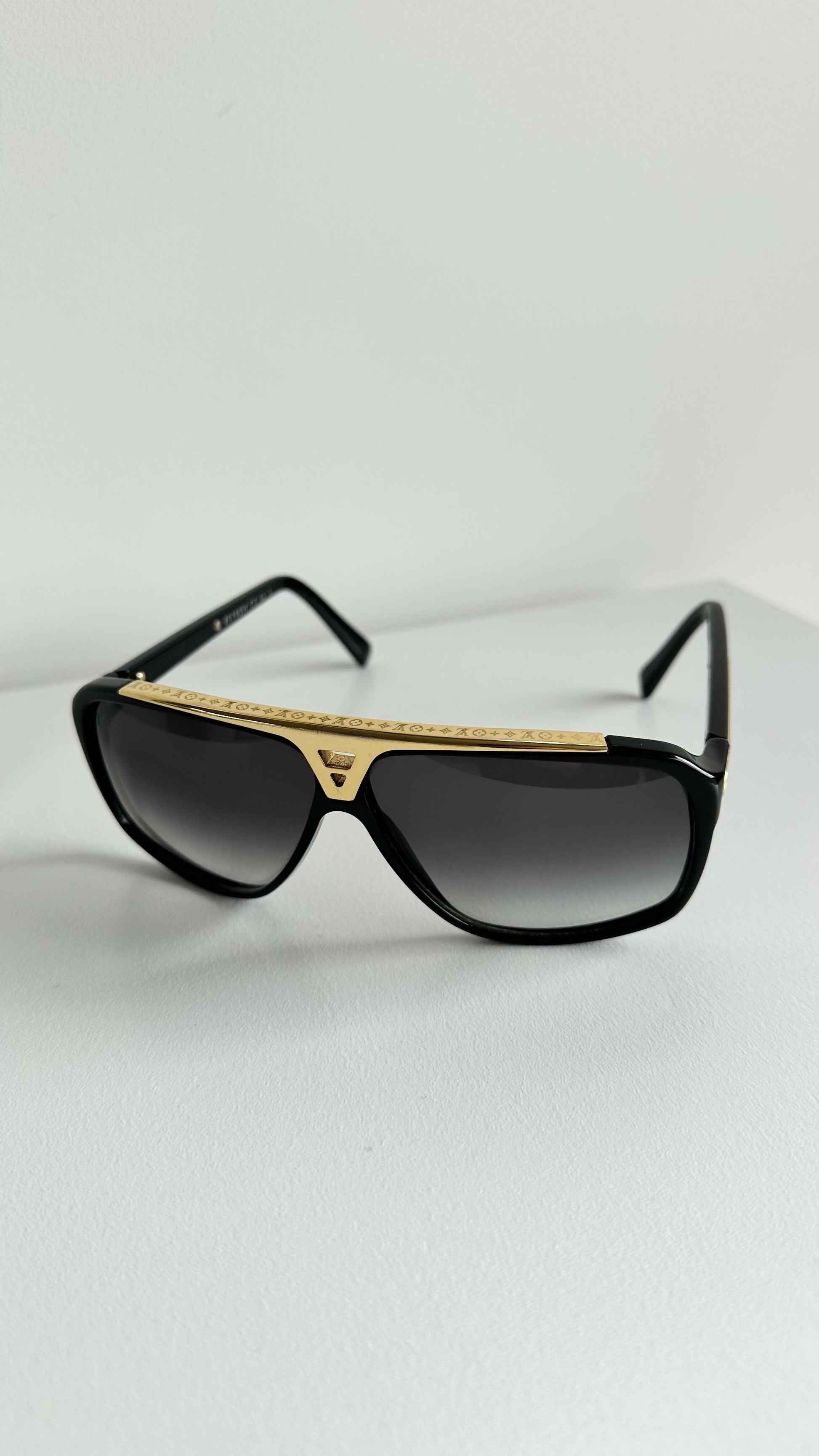 Louis Vuitton Evidence Noir W Sunglasses by EXCHANGE STORE, featuring a gold bar across the top, are displayed on a white surface against a plain white background.