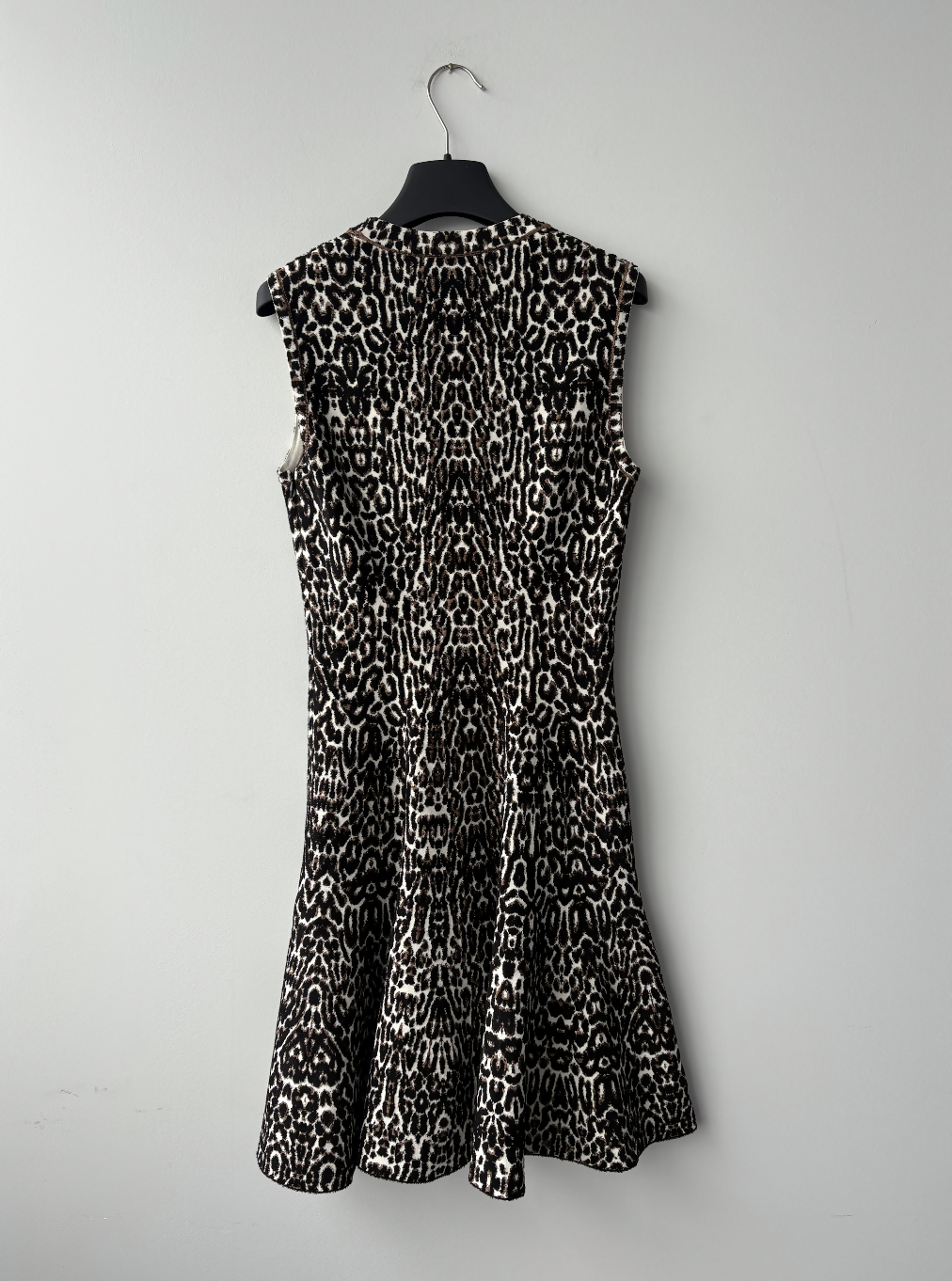 The Alaia Leopard-print Jacquard Minidress by EXCHANGE STORE features a sleeveless fitted top and flared skirt, shown on a black hanger against a light gray wall.