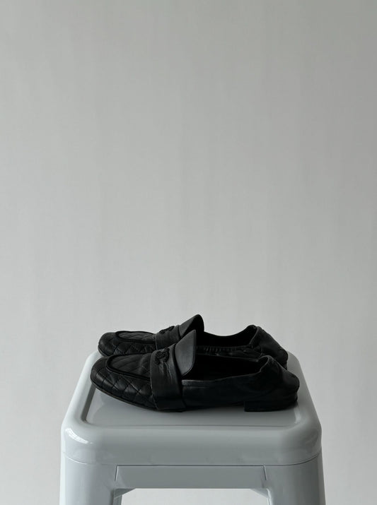 A pair of Vintage Chanel Loafers from EXCHANGE are neatly placed on a white plastic stool against a plain, light gray background.