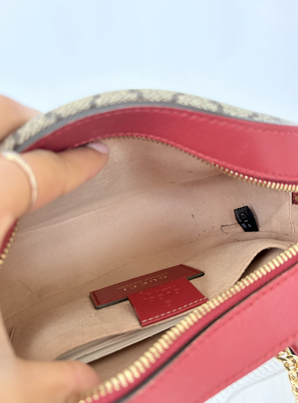 A close-up of a hand holding open the Gucci Kingsnake Heart Mini GG Supreme Chain Crossbody Bag by EXCHANGE STORE, revealing its beige interior, Gucci leather tag, black label, gold zipper, and patterned trim.