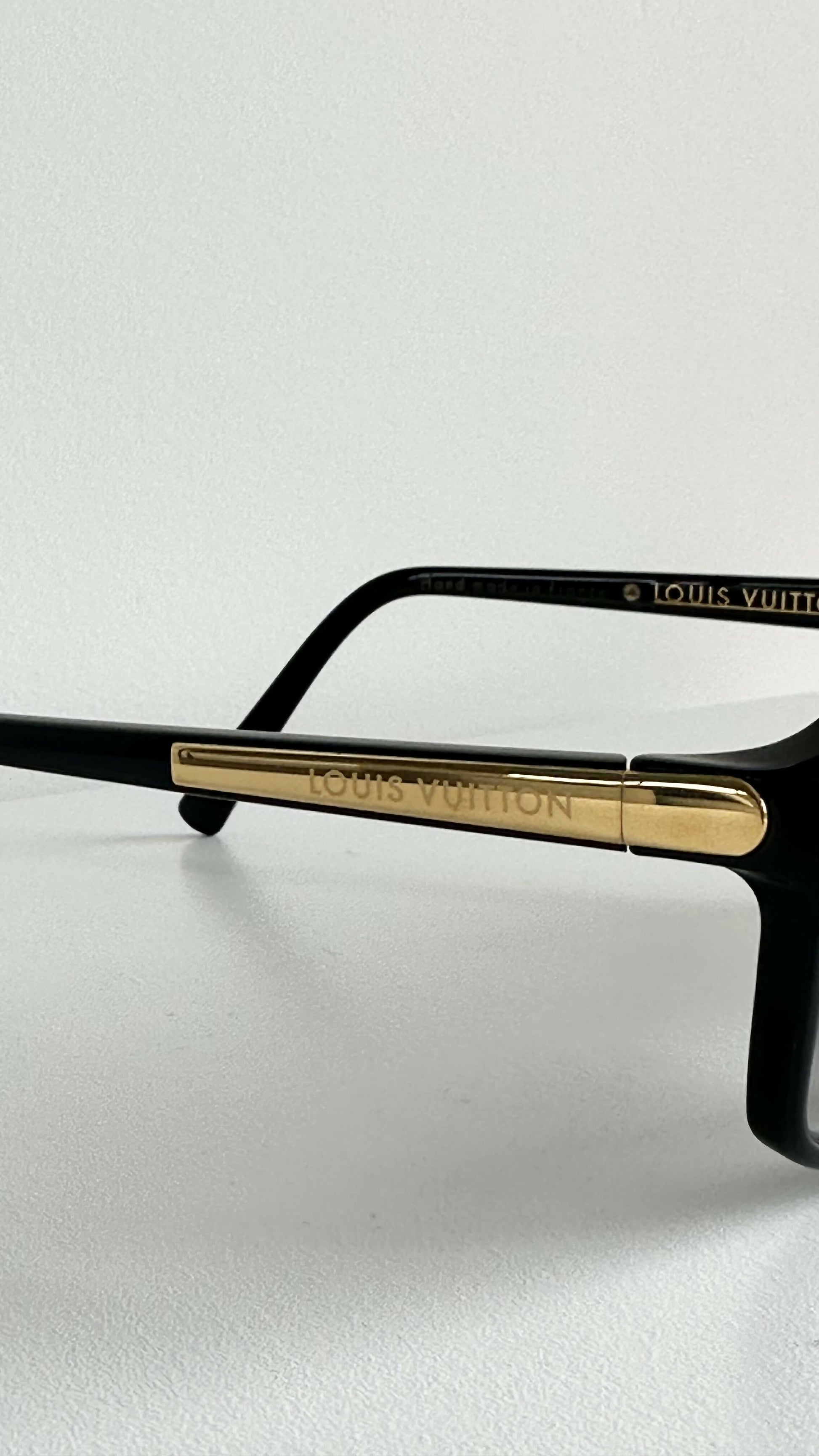 A close-up of Louis Vuitton Evidence Noir W Sunglasses from EXCHANGE STORE, featuring black frames with gold accents and the signature Louis Vuitton logo engraved on the side, showcasing luxury style.