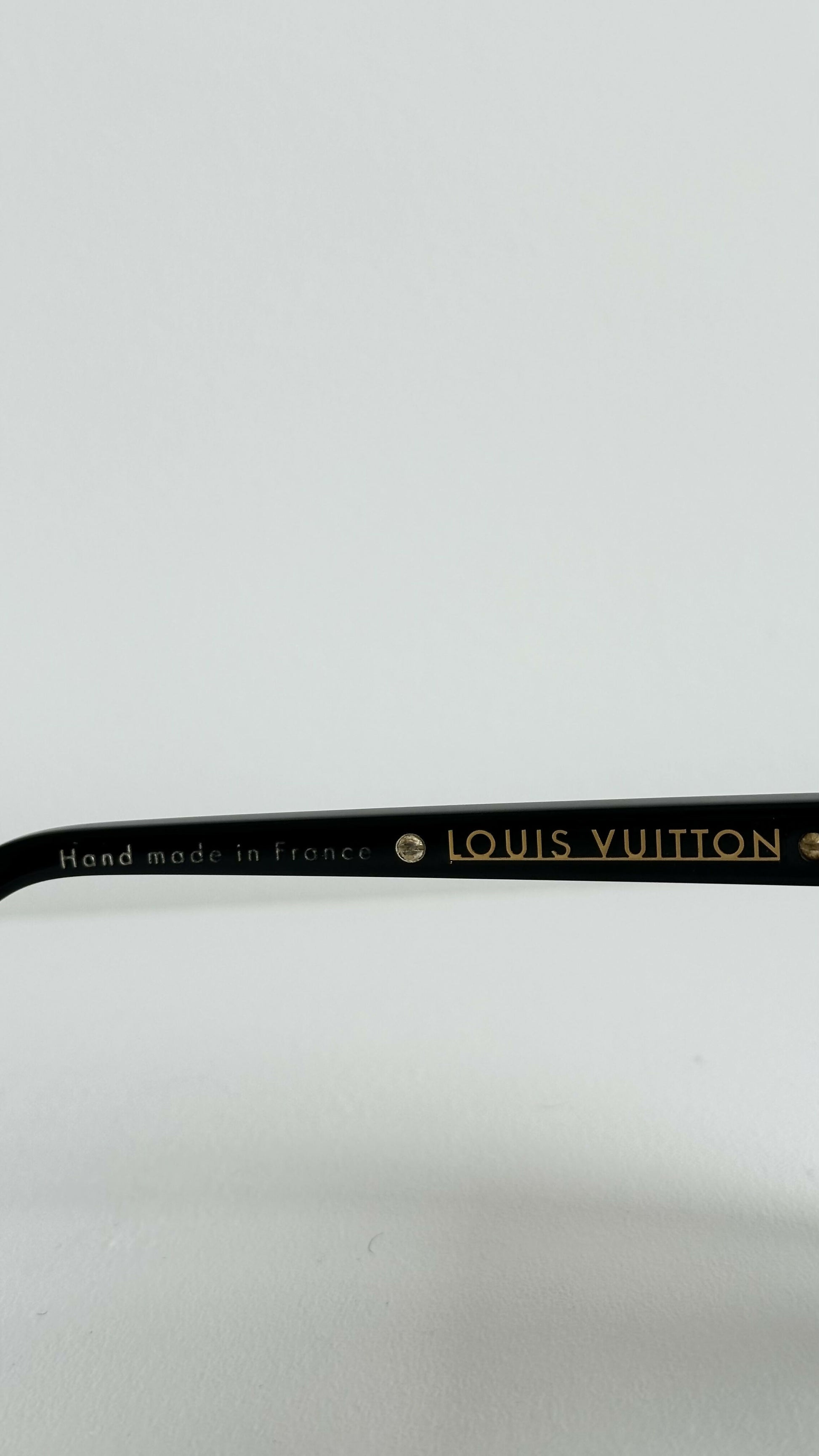 Close-up of the black arm of Louis Vuitton Evidence Noir W sunglasses by EXCHANGE STORE, showing gold "LOUIS VUITTON" lettering and "Hand made in France" against a plain white background.