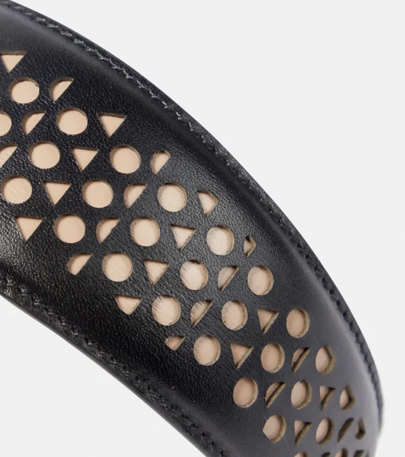 A close-up of the Alaïa Vienne Laser-Cut Leather Headband from EXCHANGE STORE, featuring black leather with circular and triangular cut-outs that reveal beige material beneath.