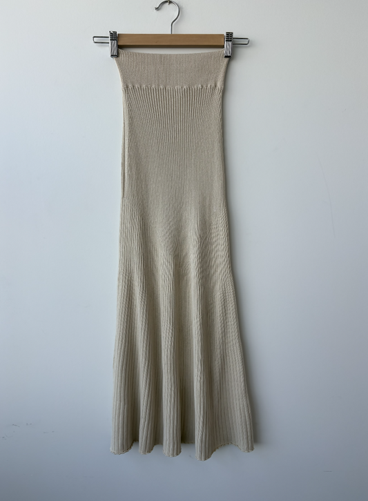 The Dadelszen Beiged Ribbed Knit Skirt by EXCHANGE STORE, featuring a high fitted waist and flared hem, hangs on a wooden hanger against a plain white wall—an ideal addition to any luxury wardrobe.