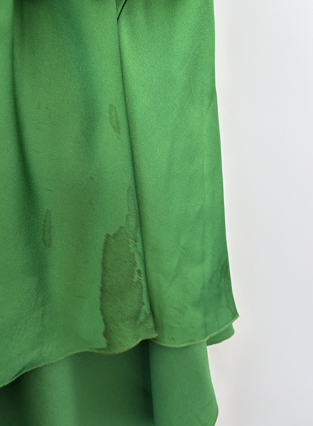 A close-up of the Victoria Beckham Resort 2022 Green Cami Slip Dress by EXCHANGE STORE shows visible wet stains on its satin surface against a plain white background.