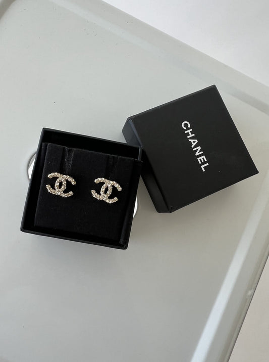 A pair of EXCHANGE Chanel Crystal Pearl Studs earrings in a black box, with the branded lid and Authenticity Card beside them on a light gray surface.