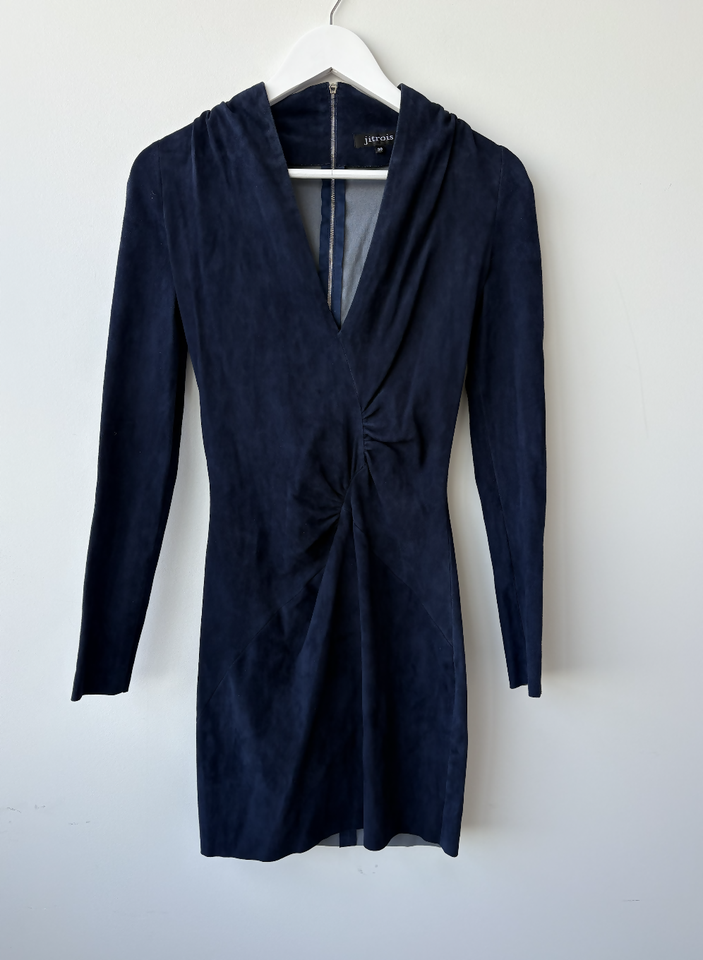The EXCHANGE STORE Jitrois Navy Velvet Longsleeve Mini Dress, featuring a fitted silhouette and gathered waist, exudes subtle rock-chic vibes as it hangs on a white hanger against a plain light-colored wall.