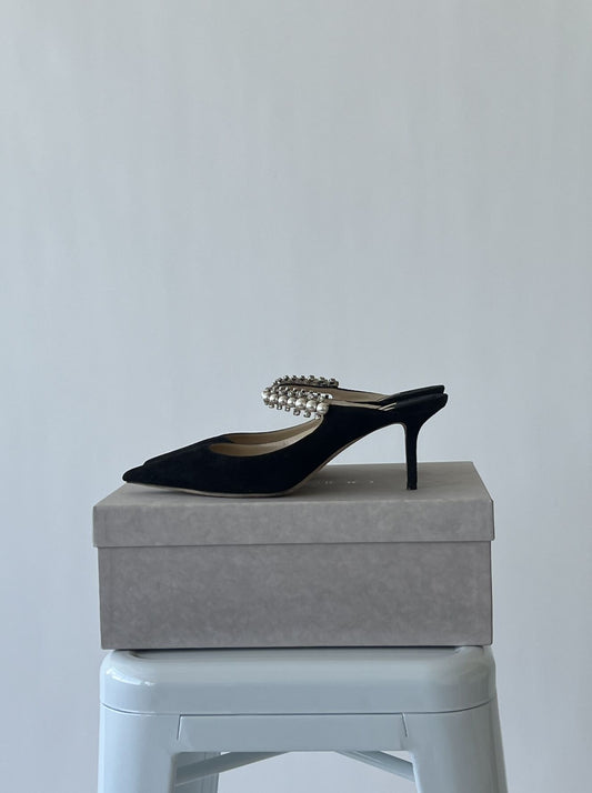 The EXCHANGE JIMMY CHOO Suede Bing 65 Pumps, black with a pearl-embellished strap and 2.75" heel (EU 40), are displayed on a gray box atop a light stool against a plain background.