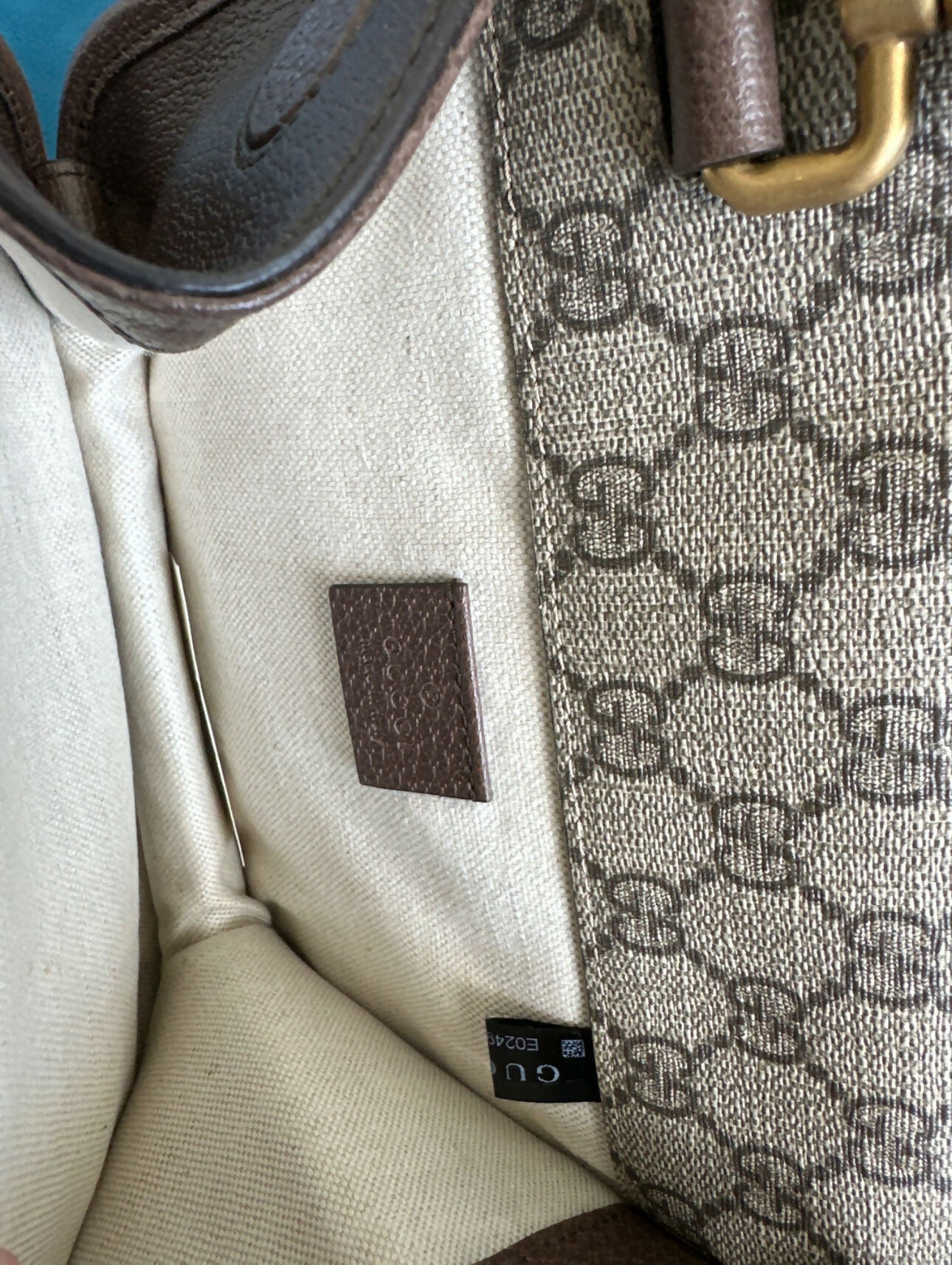 Close-up of the Gucci Neo Vintage messenger bag by EXCHANGE STORE, featuring beige fabric lining, a brown leather tag inside, and a GG monogram patterned exterior with part of a gold metal clasp visible.