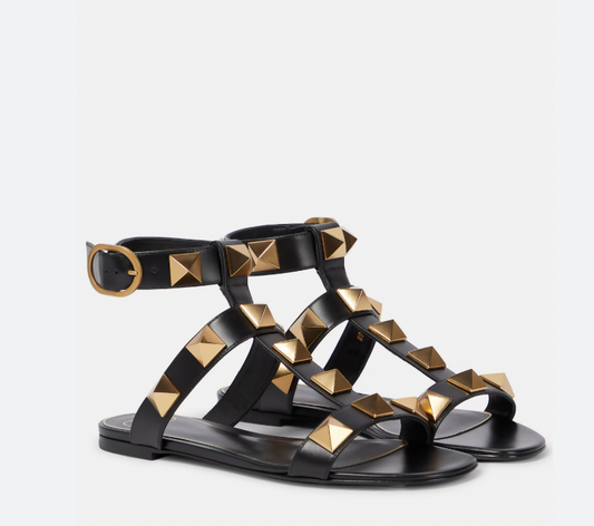 The EXCHANGE STORE Valentino Garavani Roman Stud Sandals Black - FULL SET features wide black leather straps with large gold pyramid studs and a gold ankle buckle, inspired by the iconic Roman Stud design.