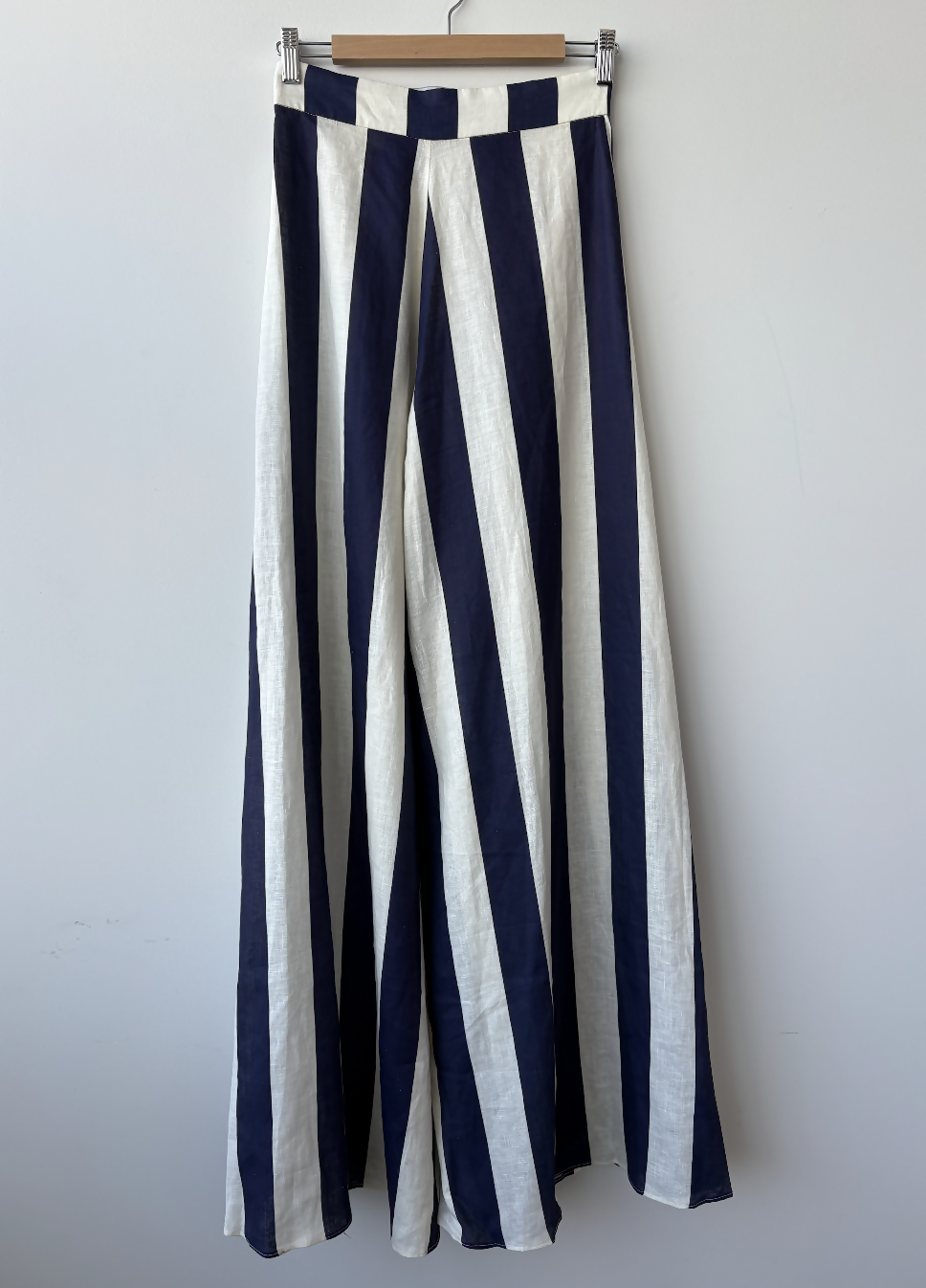 The EXCHANGE STORE Paper London Navy Stripe Wide Leg Pant hangs on a wooden hanger against a plain white wall.