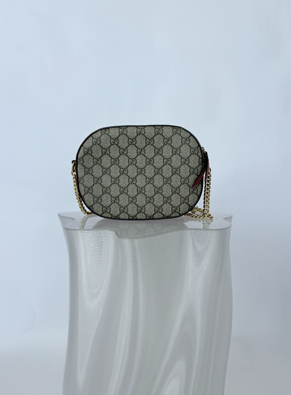 The EXCHANGE STORE Gucci Kingsnake Heart Mini GG Supreme Chain Crossbody Bag - FULL SET, featuring the beige and brown monogram, is displayed on a translucent textured pedestal against a plain white background.
