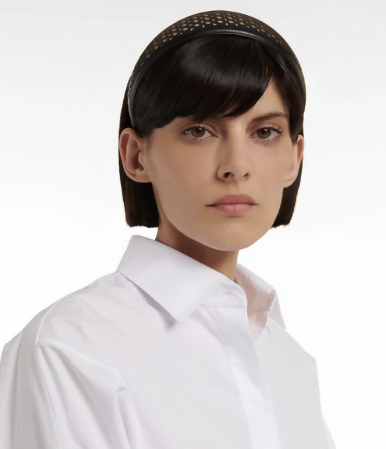 A woman with short dark hair wears the Alaïa Vienne Laser-Cut Leather Headband - FULL SET from EXCHANGE STORE and a white collared shirt, looking directly at the camera against a plain background.
