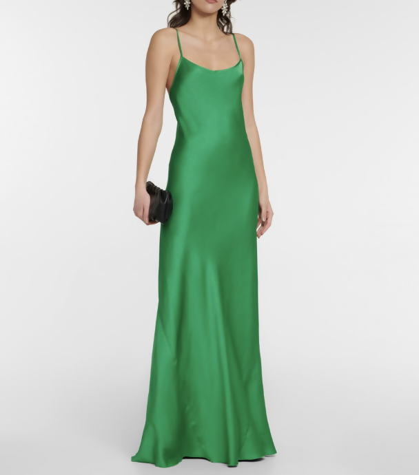 A woman wears the Victoria Beckham Resort 2022 Green Cami Slip Dress by EXCHANGE STORE, a long, sleeveless satin dress with thin straps, holding a small black clutch against a plain white background.