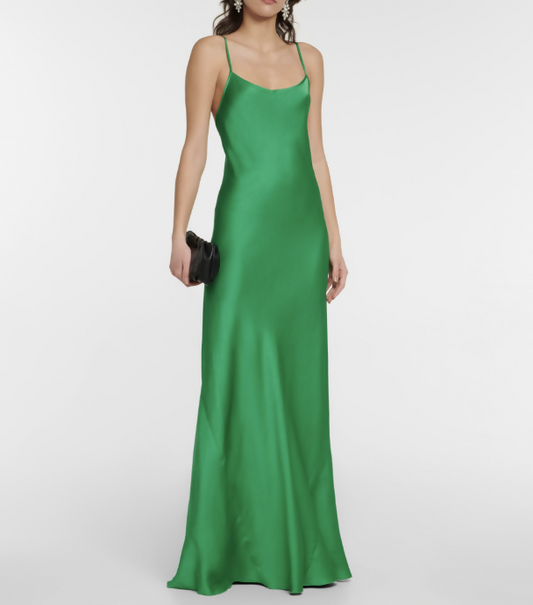 A woman wears the Victoria Beckham Resort 2022 Green Cami Slip Dress by EXCHANGE STORE, a long, sleeveless satin dress with thin straps, holding a small black clutch against a plain white background.