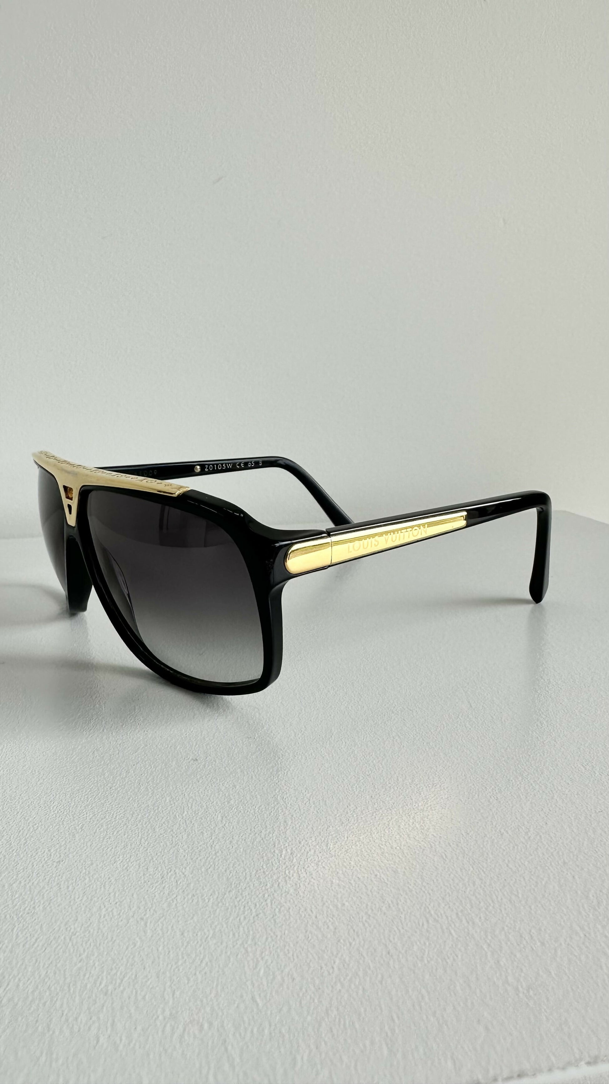 Louis Vuitton Evidence Noir W Sunglasses by EXCHANGE STORE with dark tinted lenses rest on a white surface, the Louis Vuitton logo visible on the arms.