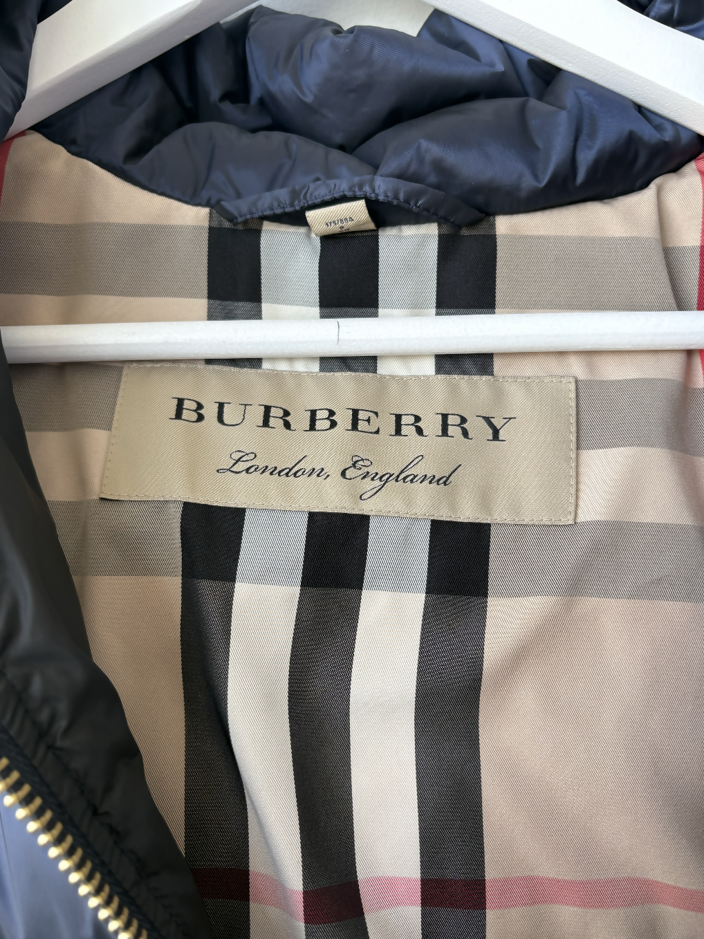Close-up of an EXCHANGE STORE Burberry Puffer with Fur Hood label showing "BURBERRY London, England" text and the signature beige, black, and red check inner lining of this luxury winter jacket.