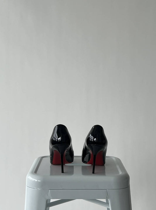 A pair of Christian Loubiton Black Pump heels by EXCHANGE (size 36.5) is displayed side by side on a light gray stool against a plain, light background.