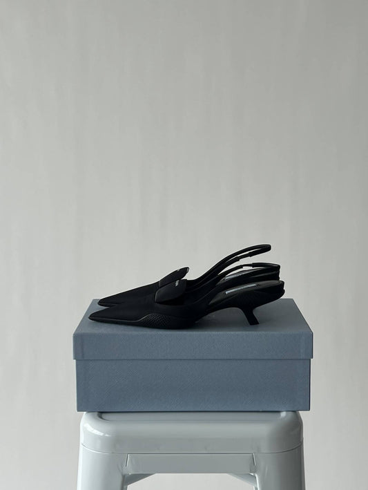 A pair of black EXCHANGE Prada shoes rests neatly on a closed light blue shoe box, positioned on a white stool against a plain light gray background.