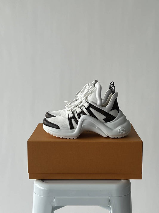 The LV Archlight Sneaker by EXCHANGE, in white and black, size 38, is displayed atop a brown shoe box on a white stool set against a plain light gray background.