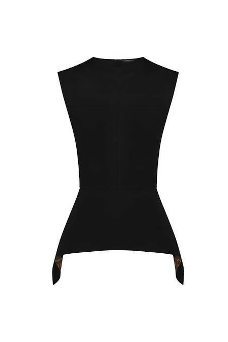 The EXCHANGE LV Peplum Shirt features a sleeveless black design with a fitted waist, pointed asymmetrical hem, and logo detail in smooth scuba jersey, shown against a white background.