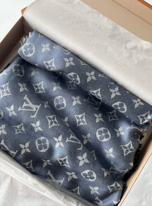 The EXCHANGE Louis Vuitton Monogram Scarf in blue with white patterns is neatly folded inside a box lined with white tissue paper.
