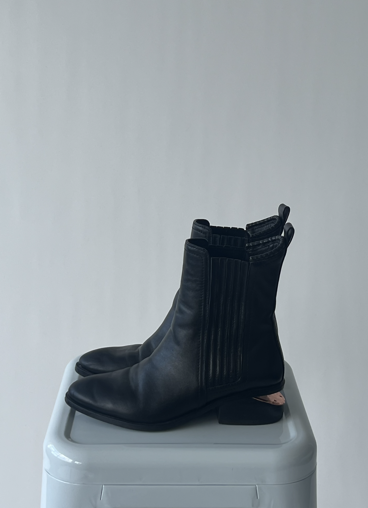 A pair of gently worn black leather EXCHANGE Alexander Wang Anouk Boots with elastic sides and replaced soles sits on a white rectangular surface against a plain light gray background.