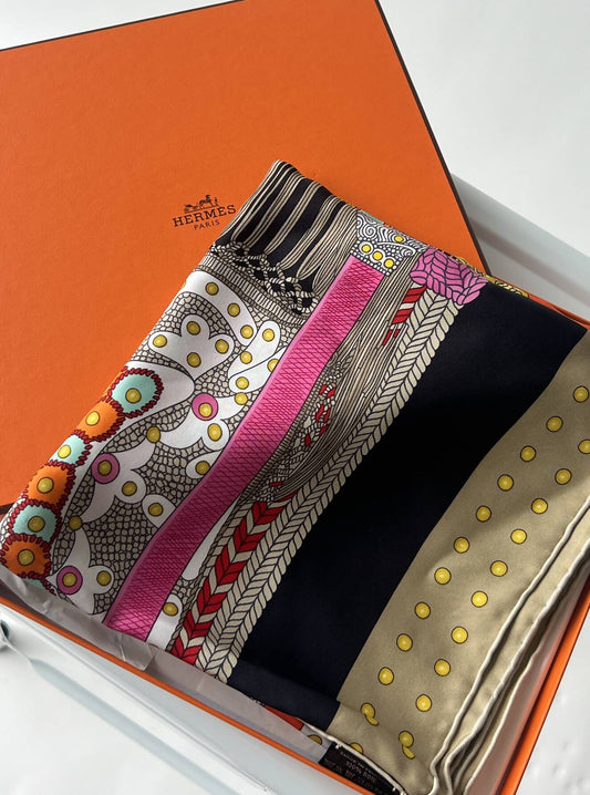 A vibrant EXCHANGE Hermès Silk Scarf, adorned with pink, black, beige, and orange patterns, is elegantly folded in an open orange gift box on a white surface—a perfect chic silk wrap.